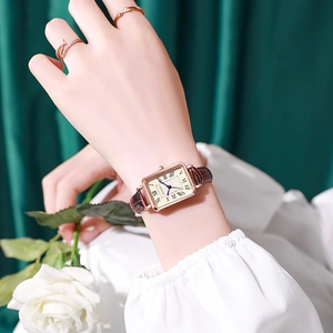 Close-up of vintage rectangular quartz watch with brown leather strap holding a white rose