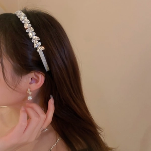 Close-up of sparkling rhinestone headband and floral pearl earrings on model