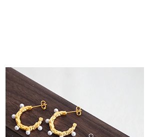 Detail view of gold C-shaped earrings with irregular texture and white pearl embellishments