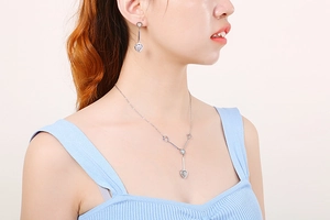 Silver heart-shaped pendant necklace and earring set shown on model in close-up view