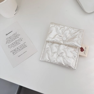 Close-up of heart-quilted white fabric pouch with snap button and brand woven label