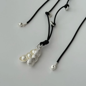 Macro shot of silver pea pod pendant with white pearls on a black rope necklace