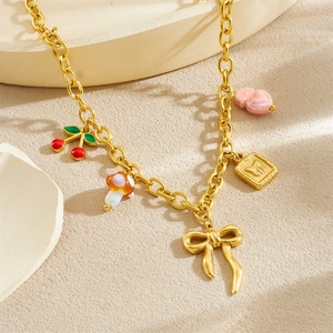 Gold-plated chain necklace featuring cherry, mushroom and bow charms on beige surface
