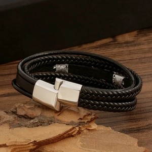 Detailed view of black woven lizard leather bracelet with silver magnetic buckle on wood