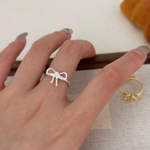Close-up of minimalist S925 sterling silver bow ring worn on hand with gold variant background