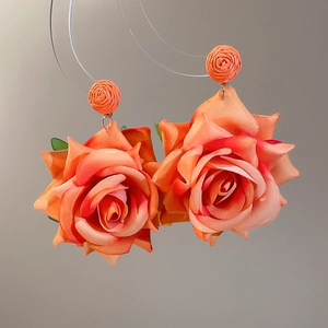 Detail of large fabric rose earrings with realistic orange gradient petals and woven studs