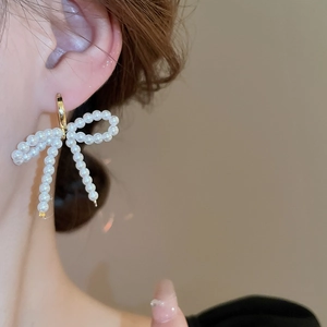 Élégantes boucles d'oreilles nœud en perles avec anneaux dorés portées par un mannequin