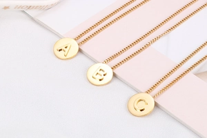 Detail of round gold initial necklaces with cutout letters A B C on minimalist pink backdrop