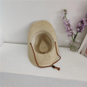 Detail of hollow woven straw cowboy hat with brown windproof rope on white surface