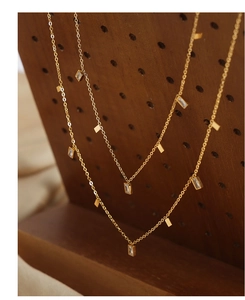 Macro detail of gold-plated titanium necklace featuring square zircons and metal charms