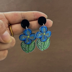Detailed shot of hand-held blue floral acrylic earrings with artistic oil painting pattern