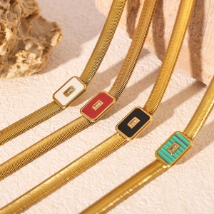Gold snake chain necklaces with colorful square shell pendants on a textured stone surface
