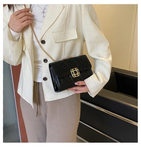 Close-up of black quilted crossbody bag with gold chain strap on a blazer model
