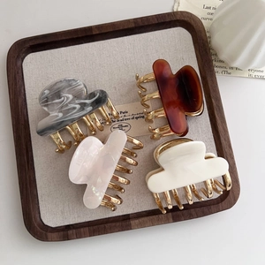 Close-up of four acetate claw clips in marble, amber and pearl white on a wooden tray