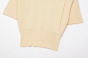 Detail of fine ribbed knit texture and hem stitching on a cream short-sleeved top