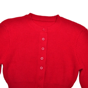 Close-up of red knit cardigan with crew neck, row of buttons, and ribbed texture detail