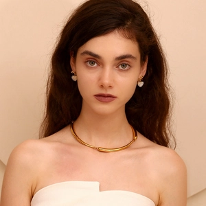 Close-up of golden heart pendant earrings and sleek metal choker on model