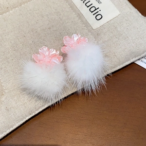 Detail of pink floral stud earrings with white fuzzy pompom drops on a wooden background