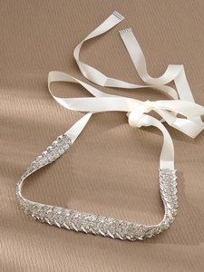 Detailed view of silver crystal bridal belt with white satin ribbon on beige background