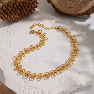 Detail of gold butterfly link necklace on white textured stone with natural pine cone decor