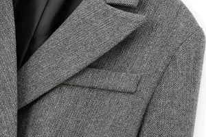 Macro shot of grey herringbone wool fabric detailing lapel and welt pocket of blazer