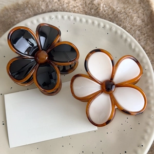 Detail of amber flower hair claws in black and beige on a vintage ceramic plate