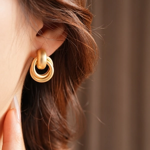 Close-up of matte golden multi-hoop earrings worn by a model in a minimalist style