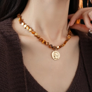 Detail of necklace with brown square beads and golden embossed portrait coin pendant