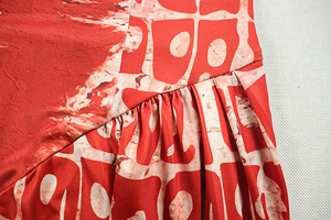 Macro detail of red geometric print dress showing fine pleated stitching and fabric texture