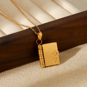 Close-up of golden book-shaped locket necklace with heart cutout on linen display