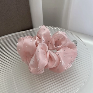 Macro detail of pink satin scrunchie featuring decorative silver rhinestones on texture