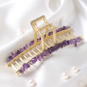 Golden alloy hair claw with purple natural crystal stones on white silk background