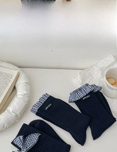 Detail of dark blue ribbed socks with gingham ruffle cuffs and logo tag on desk