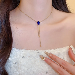 Detail of gold necklace with blue rectangular gemstone pendant and elegant tassels