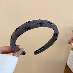 Close-up of handmade grey fabric headband featuring black bow patterns and textile label