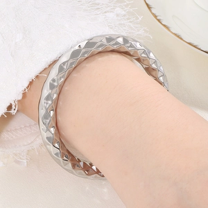 Close-up of a silver stainless steel bangle with a textured diamond pattern on a wrist