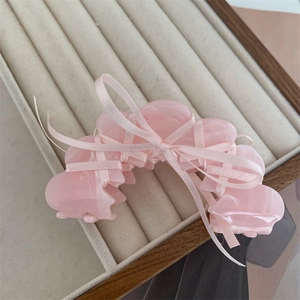 Detail shot of a pink acetate hair claw clip with silk ribbon bow on a beige tray