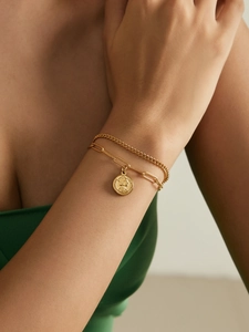 Gros plan sur le bracelet double chaîne dorée avec détail du pendentif pièce Elizabeth II