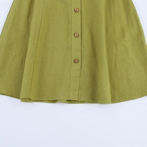 Detailed macro view of the grass green linen hemline featuring natural wooden buttons