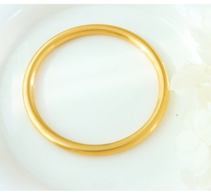 Close-up of golden solid round bangle with matte finish on white ceramic plate