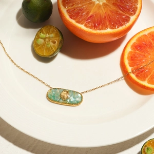 Detailed view of ocean-style seashell pendant on gold chain with citrus fruit backdrop