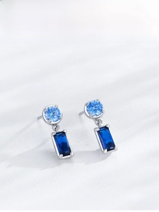 Macro shot of silver drop earrings with round light blue and square dark blue crystals