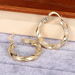 Makroaufnahme goldener gedrehter Ohrringe mit polierter und matter Textur