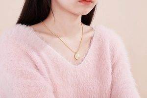 Close-up of golden Leo constellation coin necklace worn on a soft pink fuzzy sweater