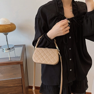 Beige quilted handbag with gold studs, worn as a crossbody bag in a stylish home setting
