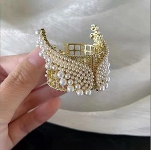 Detailed macro of golden claw clip featuring white pearls in a wing-shaped alloy design