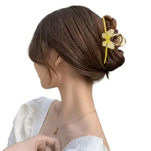Detailopname van een gele hars bloem haarklem met gouden kwastjes op een model