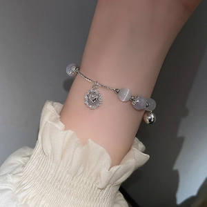 Nahaufnahme von Katzenaugen-Perlenarmband mit hohlem Herzanhänger und kleinem Glöckchen