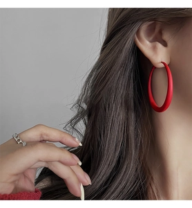 Close-up of large matte red hoop earring and silver chain ring on female model