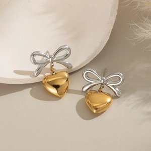 Detail of two-tone gold heart earrings with silver bow design on a soft beige background